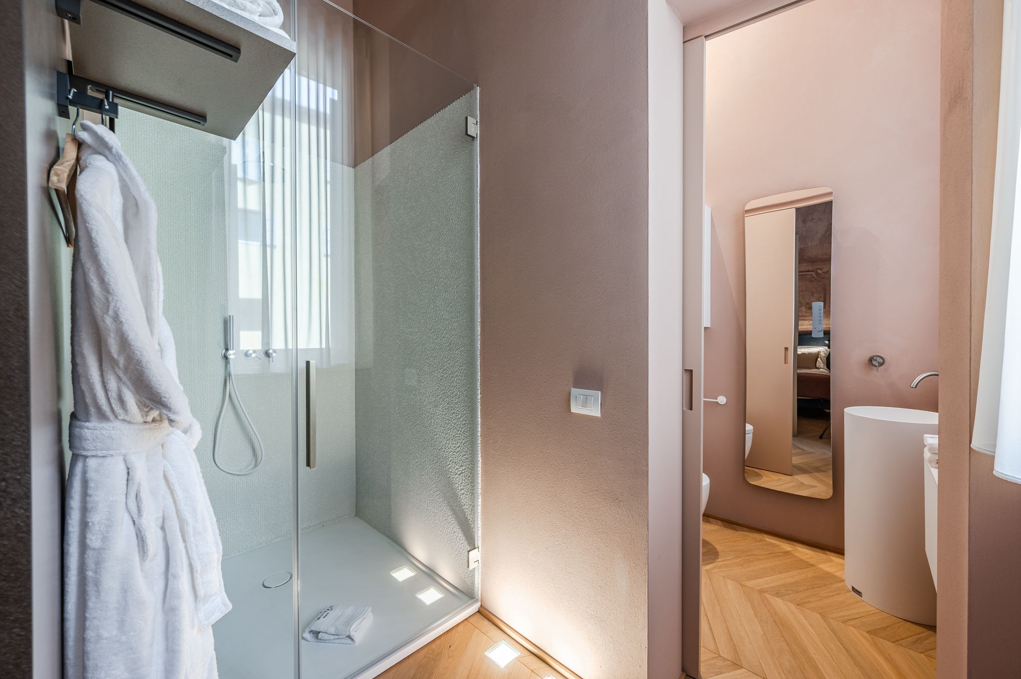 Scatto che unisce i due bagni: turchese con accappatoio e rosa con lavabo tondo