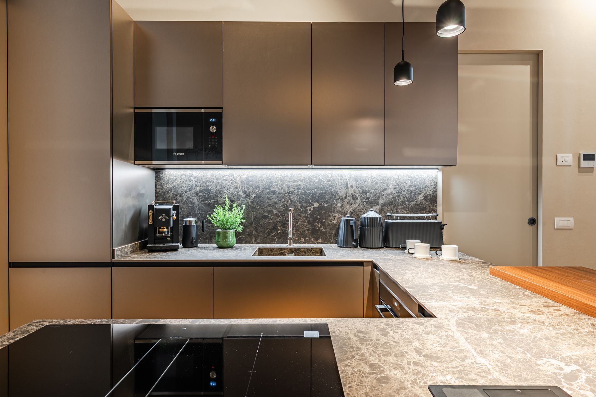 Cucina frontale con pensili tortora, backsplash in marmo retroilluminato e macchina Molinari