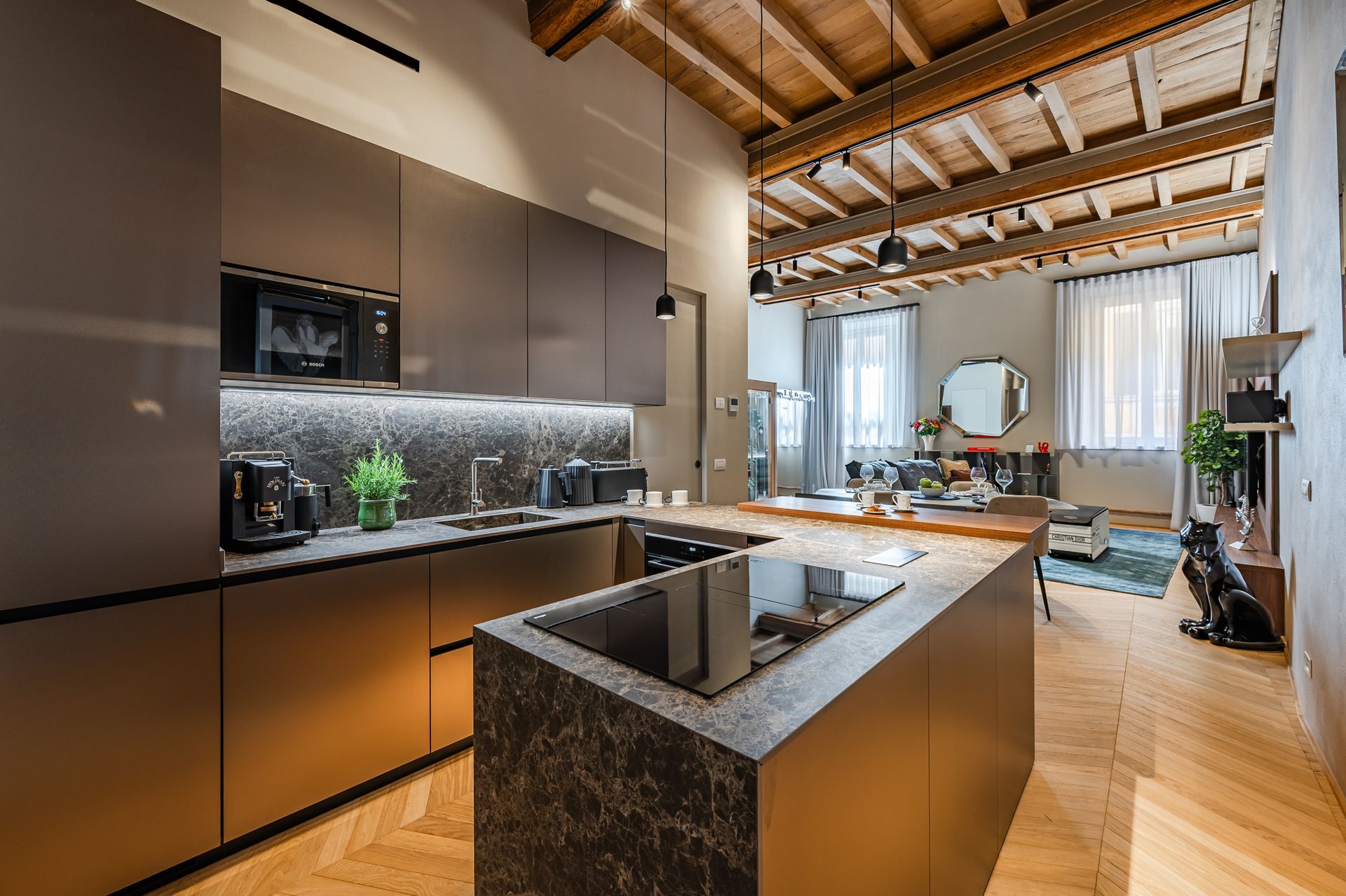 Cucina a vista sul living con isola in marmo scuro e soffitto a travi lignee