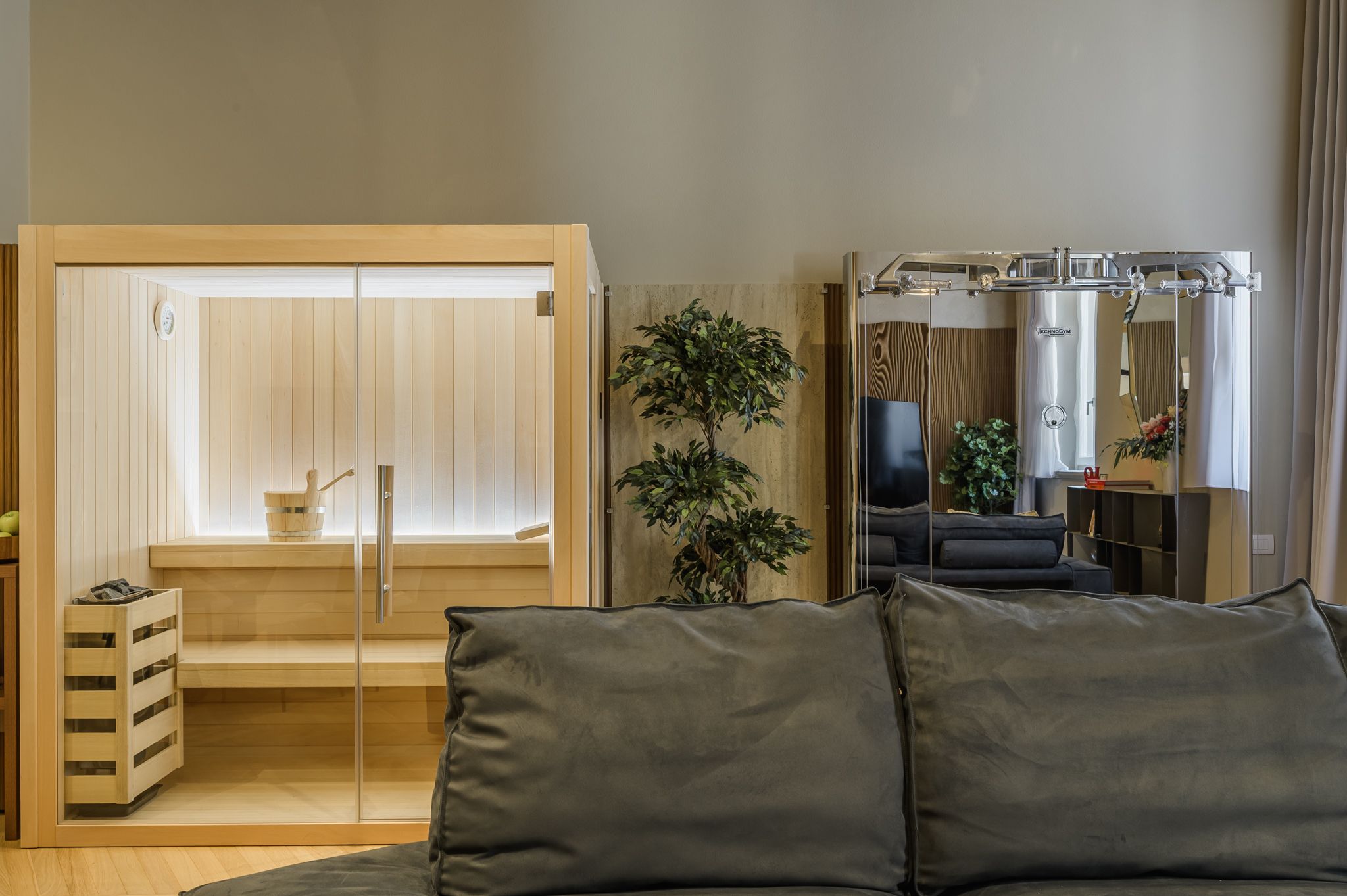 Riflesso a specchio del living con Kinesis Technogym, divano e sauna